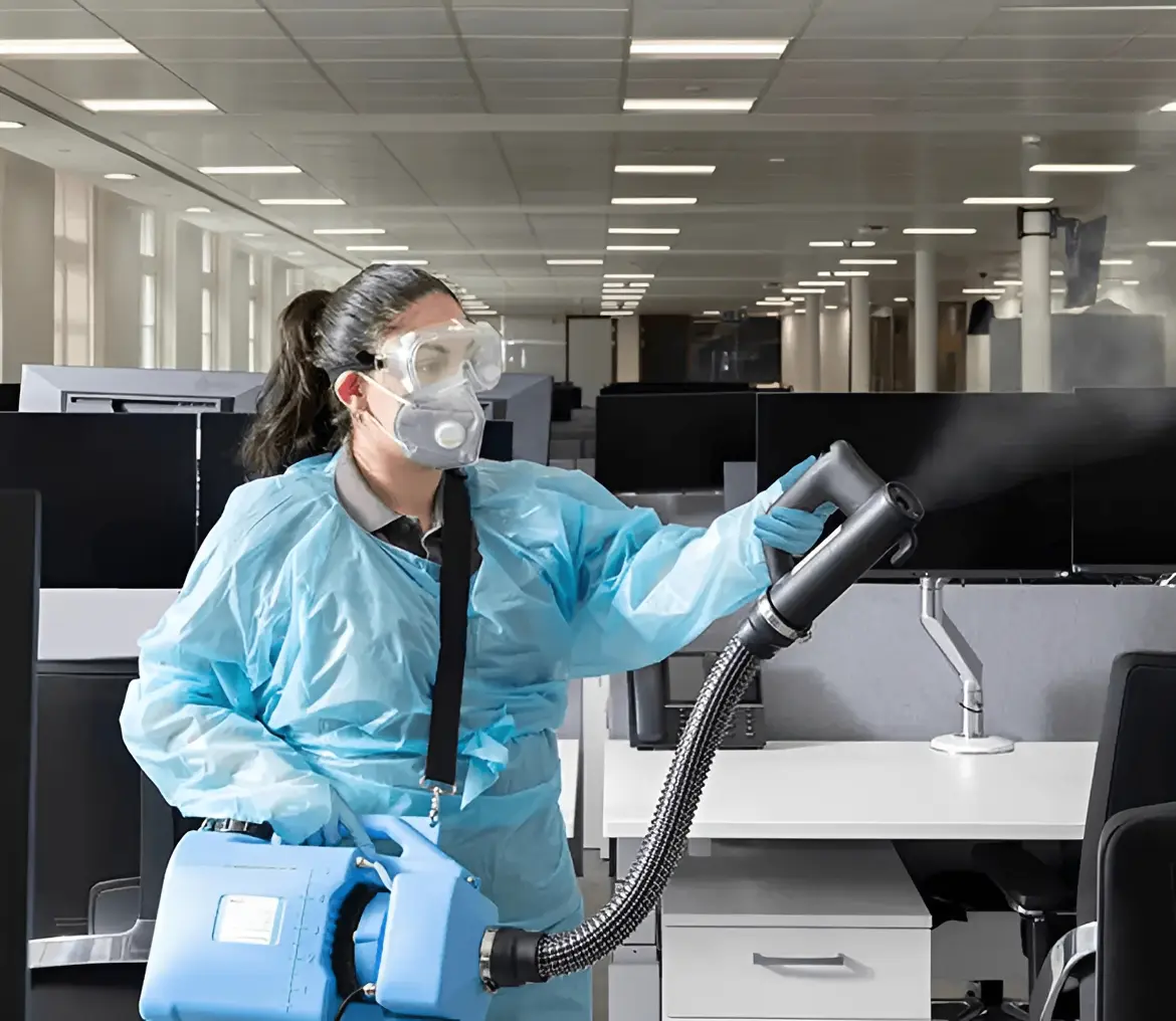 Office cleaning operative sanitising desks in modern workplace UK