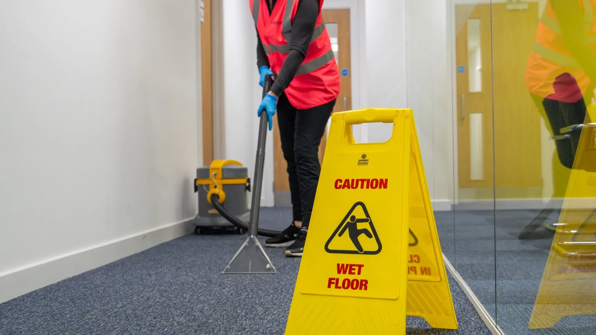 Commercial cleaner using extraction equipment with wet floor safety signage in an office environment