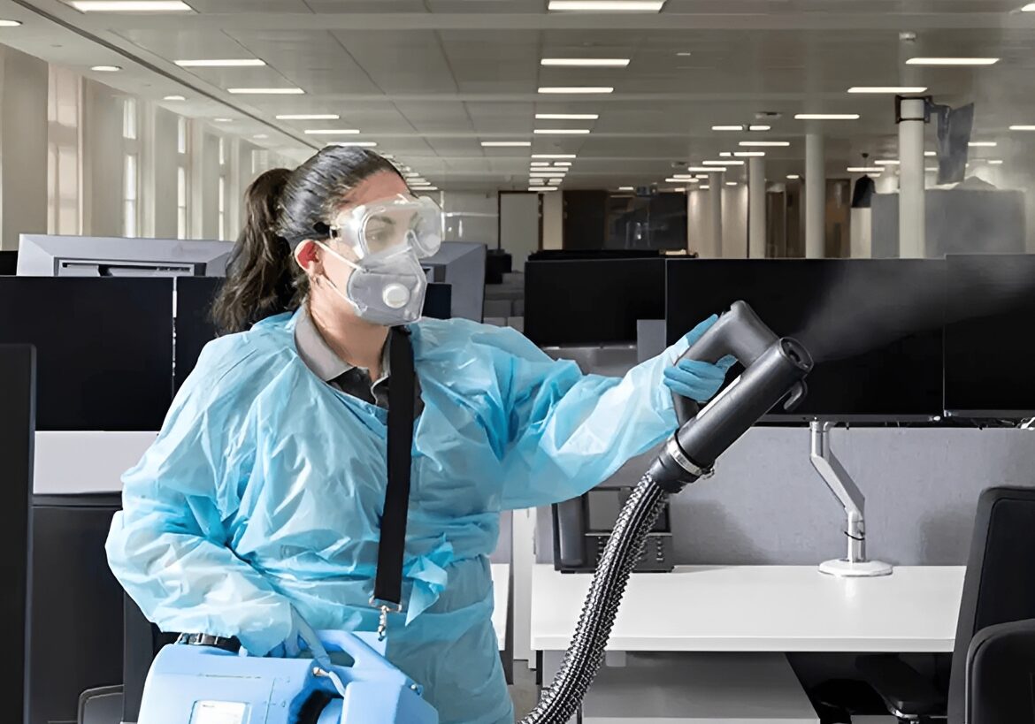 Office cleaning operative sanitising desks in modern workplace UK