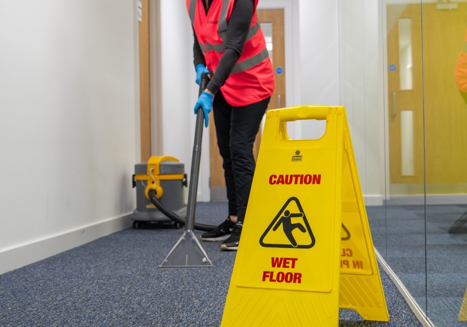 Commercial cleaner using extraction equipment with wet floor safety signage in an office environment