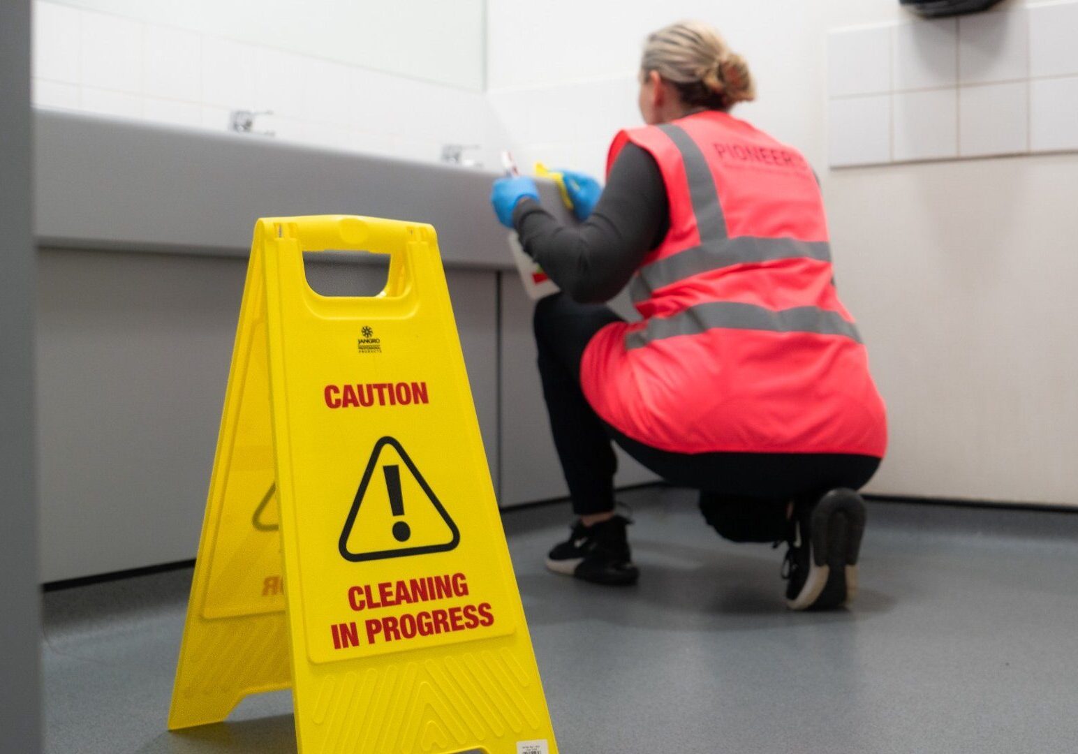Washroom cleaning in a commercial facility with safety signage and professional equipment